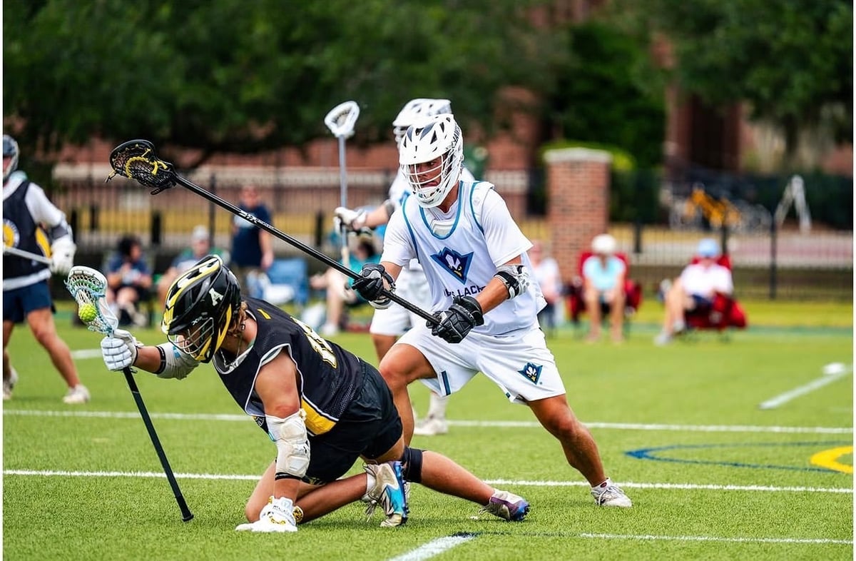 Youth lacrosse player in black jersey evading opponent in white during competitive match on grass field